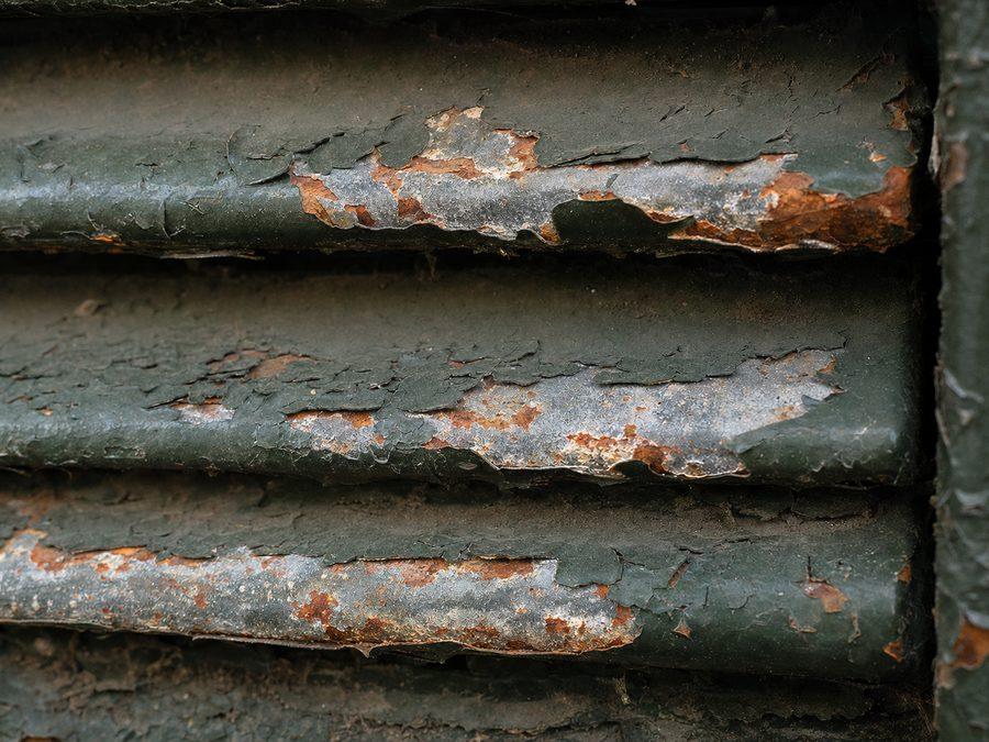 Gros plan de lames métalliques dont la peinture cloque et laisse apparaître la rouille